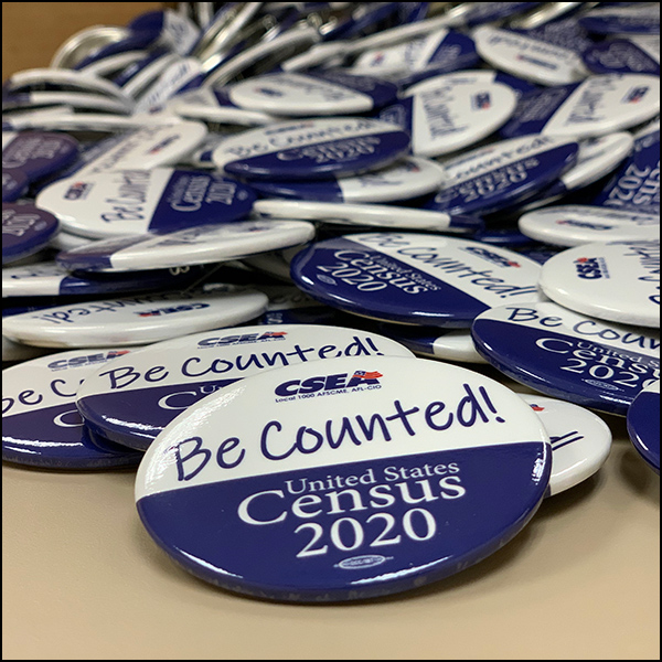 photo of a pile of census pins which the phrase "be counted!" Census 2020 on them