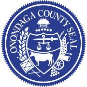 Onondaga County Seal with a blue background and white letters and images that include a sword, weights, a cow, and more